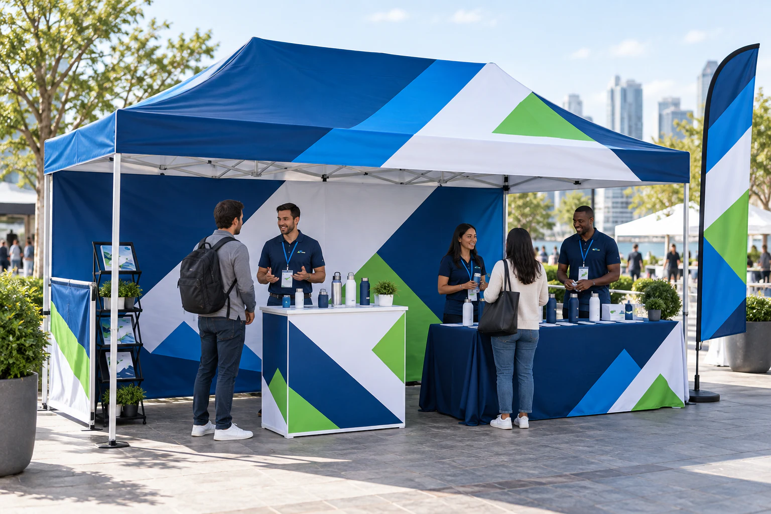 Wide blue, white and green branded event canopy with product demonstration counters, a display stand, a feather flag, staff and visitors